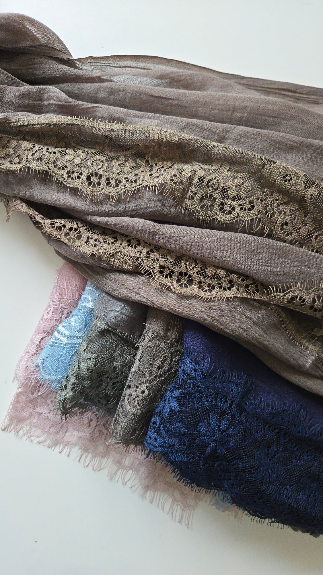 Stack of lace-trimmed fabrics in various colors on a white background