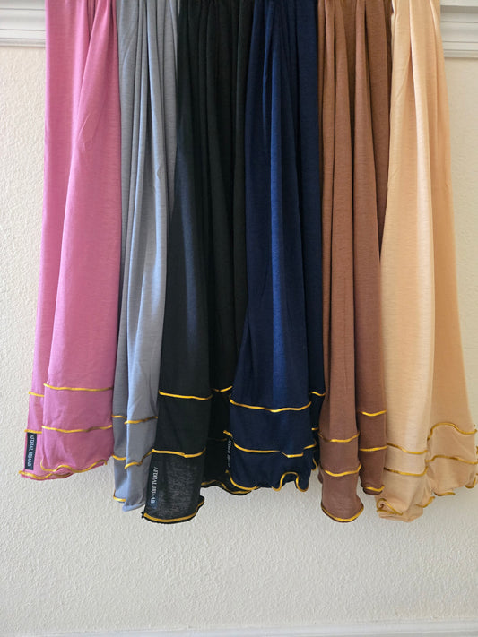Set of colorful cotton jersey hijabs with gold trim hanging against a neutral wall.