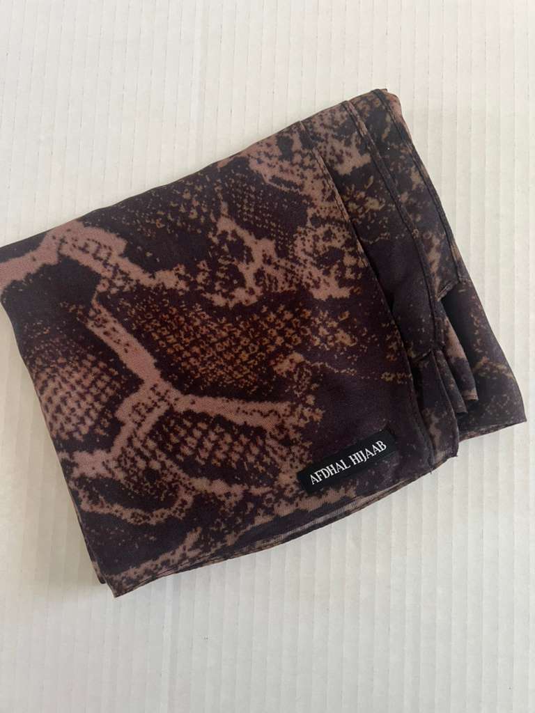 Folded modal hijab fabric with snake print on a textured white background