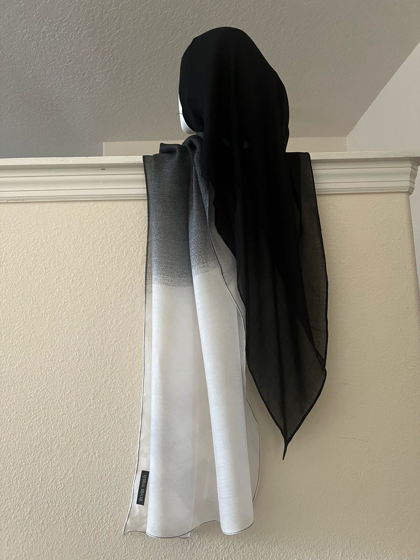 A mini ombre modal hijab in black and white, displayed hanging on a door handle.