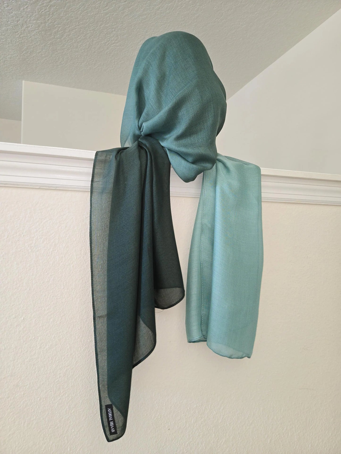 Teal scarf draped over a white window frame against a light gray wall.
